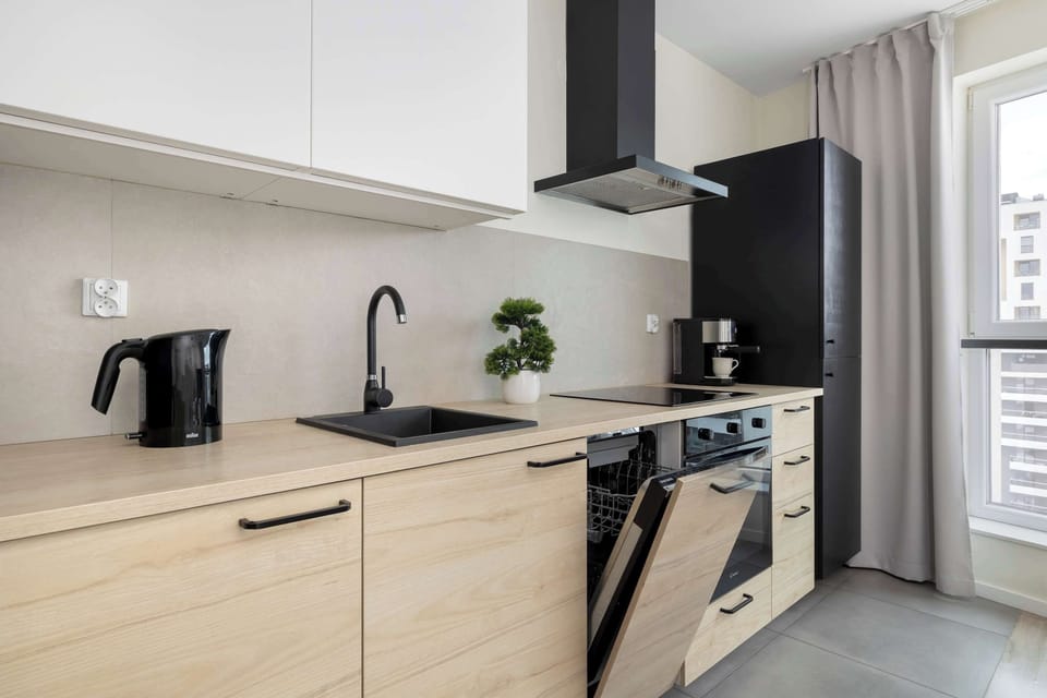 A functional kitchen area with light wooden cabinets and an open dishwasher door. A black extractor hood stands out against white upper cabinets.