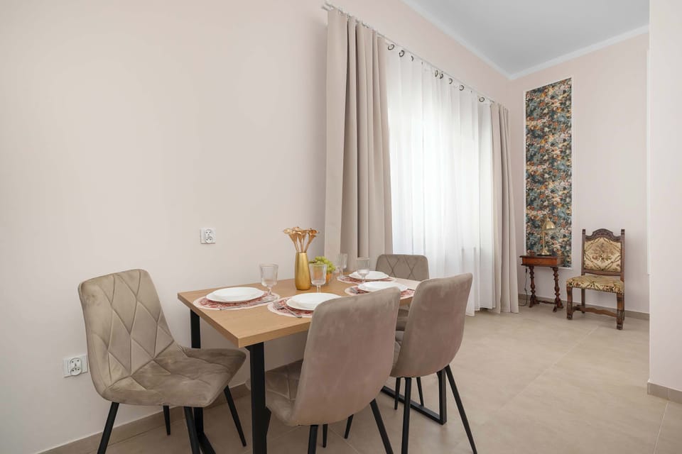 A light wood dining table surrounded by upholstered chairs sits in the middle of a spacious dining area. High ceilings, delicate sheer drapes, and vertical wall accents complete the setting.