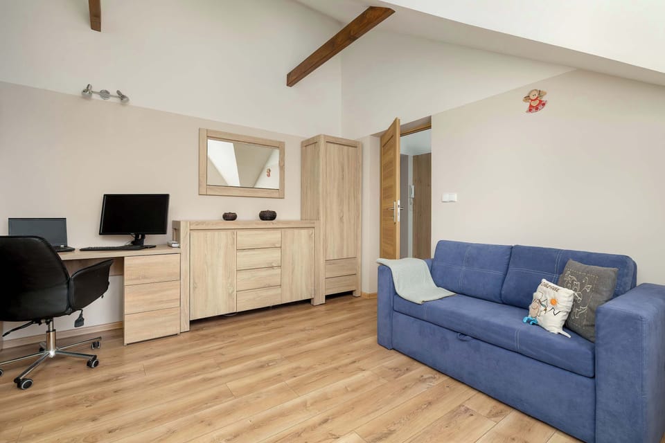 A spacious room layout combines a desk setup, wooden dressers, and a blue sofa along the wall under sloped ceilings.