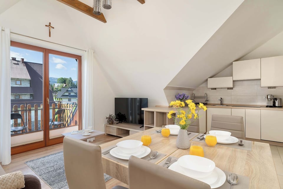 Looking from the dining set toward the open kitchen, the apartment showcases sloped ceiling beams and cozy wooden decor.