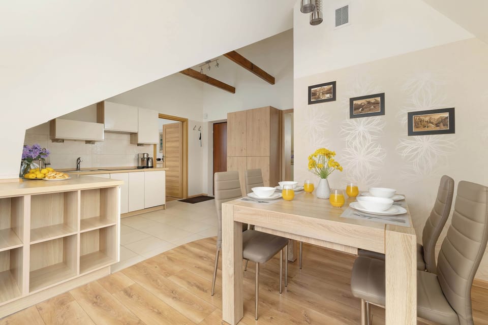 Looking across the dining table towards the kitchen, the open attic layout highlights warm wood floor finishes and sloped ceilings.