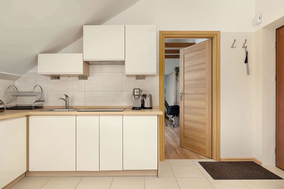 A straight-on view of the L-shaped white kitchen displays clean countertops and built-in appliances under a sloped wall.