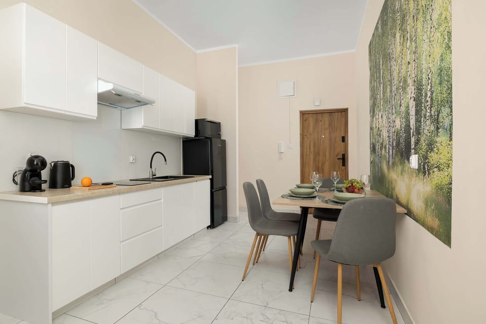 A modern kitchen connected to the dining area with a table for four guests. White cabinets and a large wall mural add a stylish touch.
