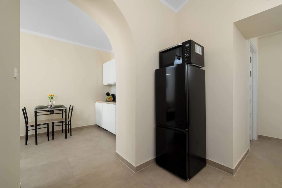 A bright dining corner with a table and chairs positioned beside the tall black refrigerator.
