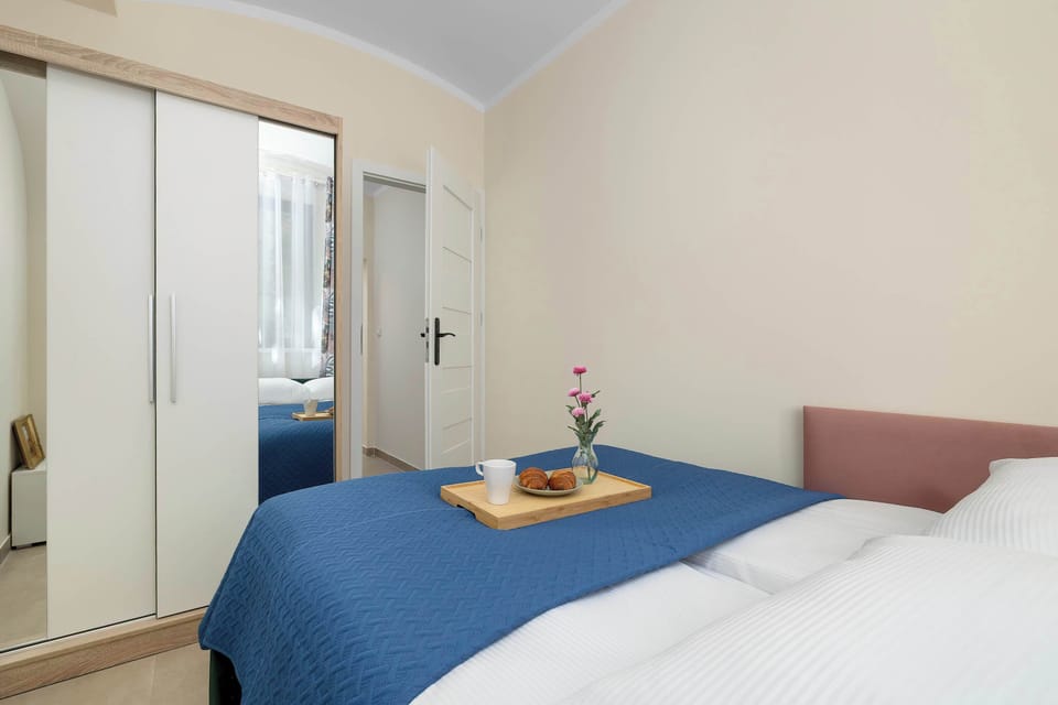 A neatly arranged sleeping area with a blue-covered bed and a small table decorated with breakfast items.