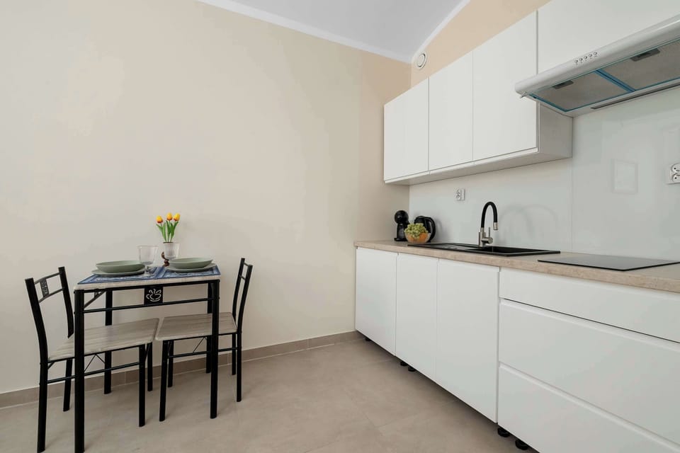 A minimalist kitchen with white cabinetry, a black refrigerator, and a small dining table.