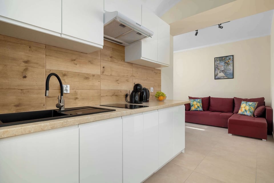 A modern white kitchen with wooden countertops, a sink, upper cabinets, and a built-in oven. The simple design creates a clean and practical cooking area.
