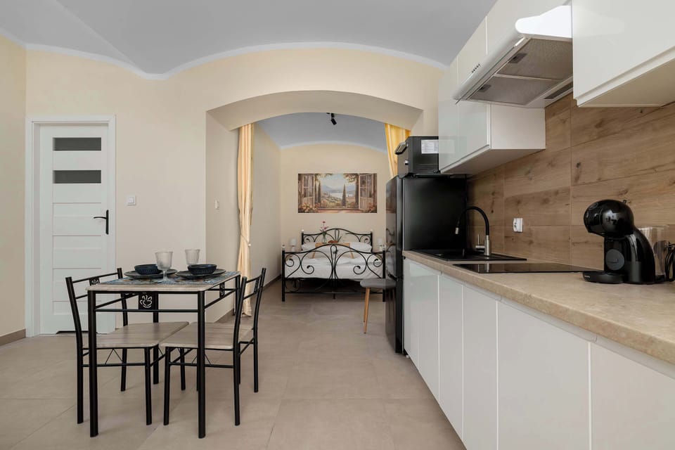 A combined kitchen and dining area with a small dining table and chairs positioned beside the white kitchen cabinets. The open layout makes the space feel bright and connected.