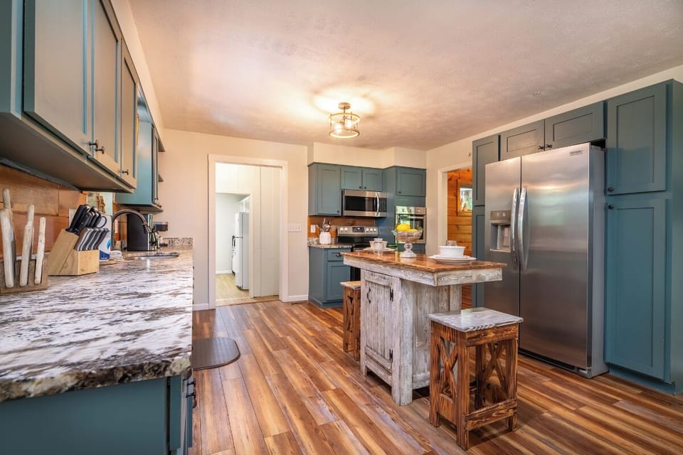 Charming kitchen blending rustic warmth with modern convenience. Blue-green cabinetry rises above rich hardwood floors, while a weathered wood island creates the perfect gathering spot for morning coffee and family meals.