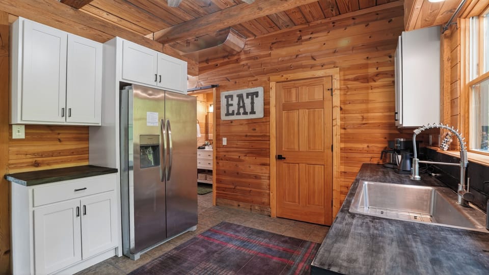 Full-size side-by-side refrigerator, ample cabinet storage, and a friendly reminder on the wall: EAT. The hallway beyond connects to the 2nd bath and laundry.