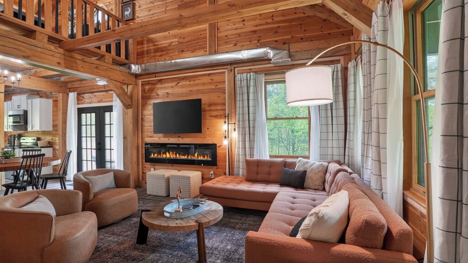 Fireplace glowing, terracotta sectional, leather swivel chairs, loft railing above, cedar walls and timber beams all around. This is the room that ends the debate about where everyone's spending the evening.