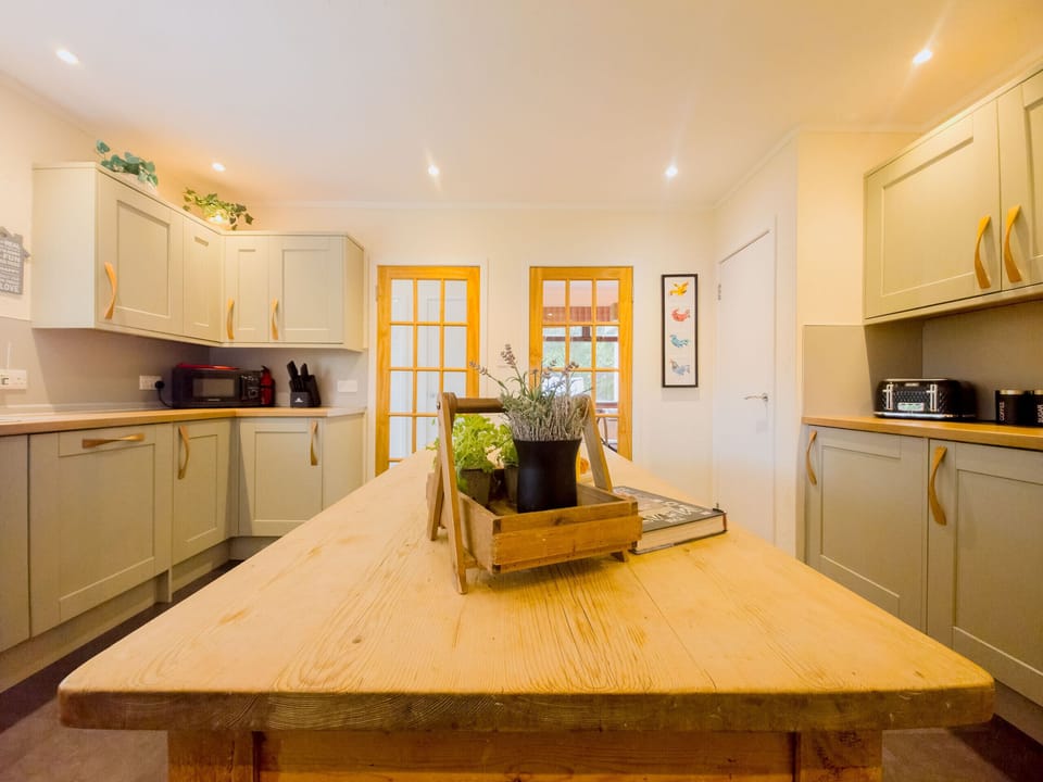 Looking across the island to the door through to the rest of the lodge. Herbs and a wooden tray sit in the middle of the table.