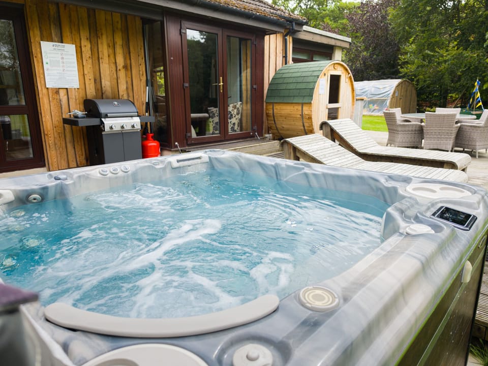 The tub bubbling away with the lodge doors just behind and the barrel sauna a few paces along. Barbecue on hand for whatever comes off the grill.