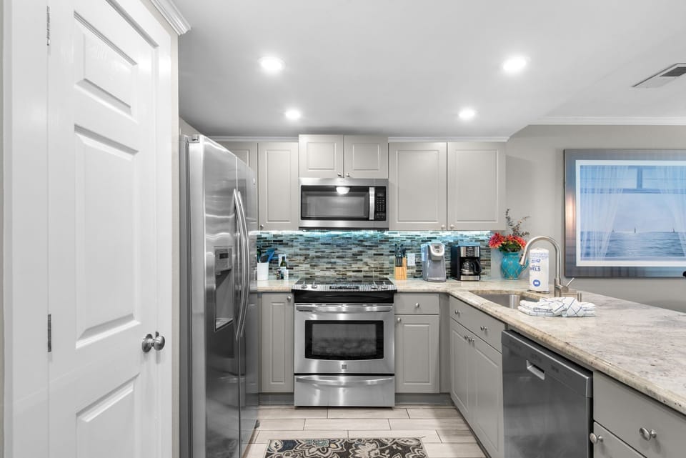 A bright, well-appointed kitchen with coastal flair—stainless steel appliances, a mosaic tile backsplash in cool blues, and plenty of counter space for making memories.