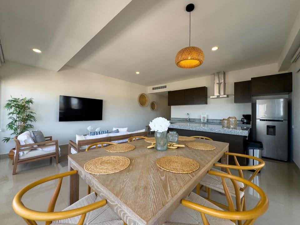Dining area with woven placemats, light wood table, yellow chairs, and rattan pendant light above.