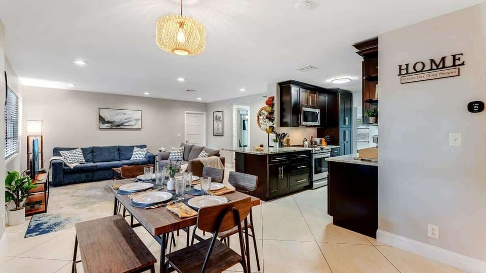 This bright, open-concept living and dining area flows right into a stylish modern kitchen—perfect for entertaining or everyday living. The space is grounded by warm beige tile floors and light, neutral walls, creating a clean and inviting vibe. 