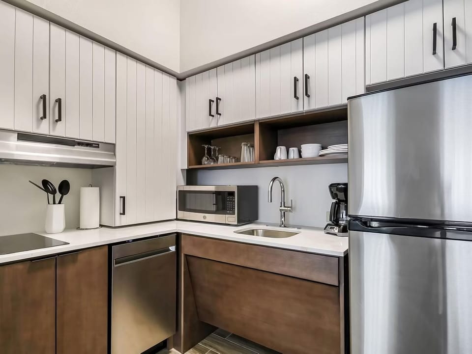 Full kitchen with light wood cabinets, electric cooktop, stainless steel appliances, and open shelving for dishes