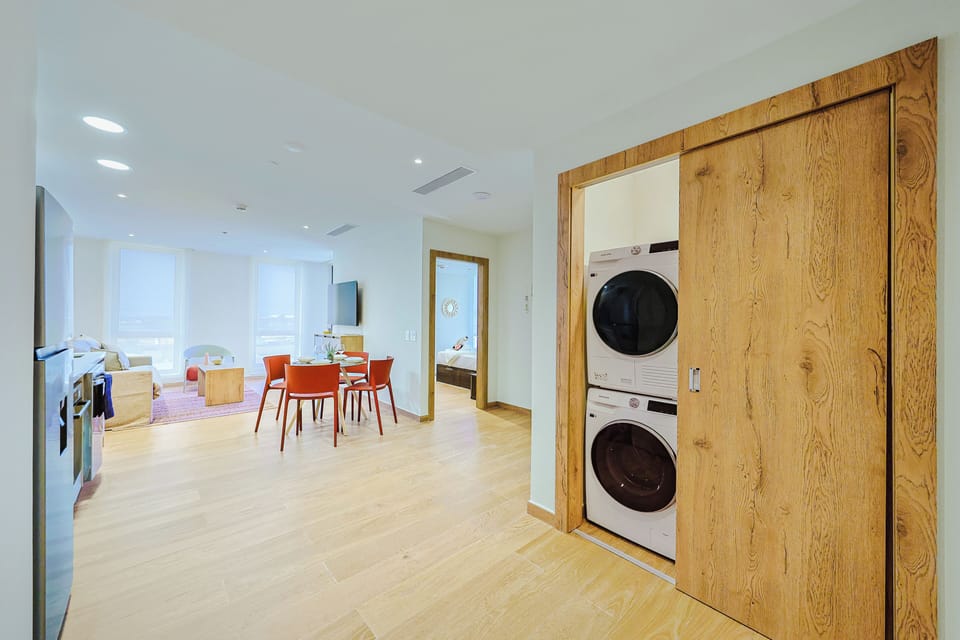 Modern convenience meets thoughtful design with an in-unit washer and dryer discreetly tucked behind sleek wood panels. Step into a bright, open living space where natural light, warm wood accents, and vibrant touches create a welcoming retreat.