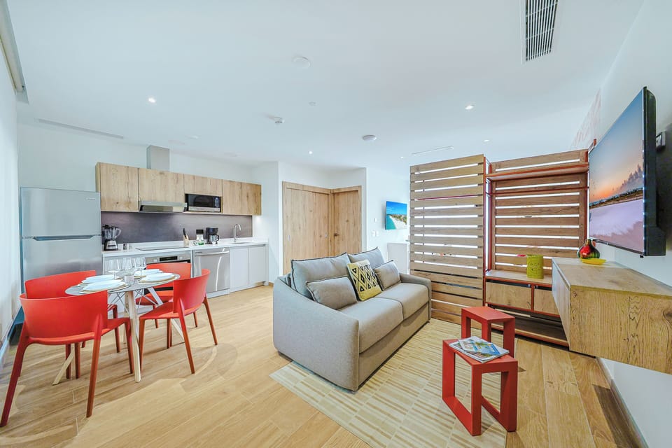Step into your bright, modern retreat with an open living and dining space bathed in natural light. Relax on the cozy sofa, enjoy meals at the vibrant red dining set, or prepare a feast in your sleek kitchenette—all in one inviting, stylish layout.