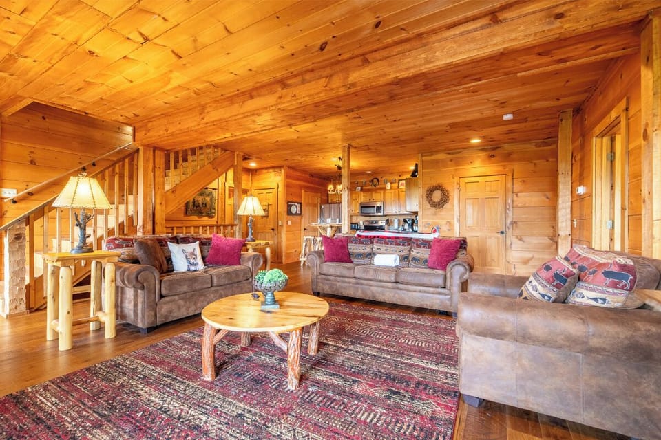 Gather around the rustic coffee table in this warm, wood-paneled living area. You'll love the cozy lamps, plush sofas with colorful cushions, and inviting open layout that flows into the kitchen.