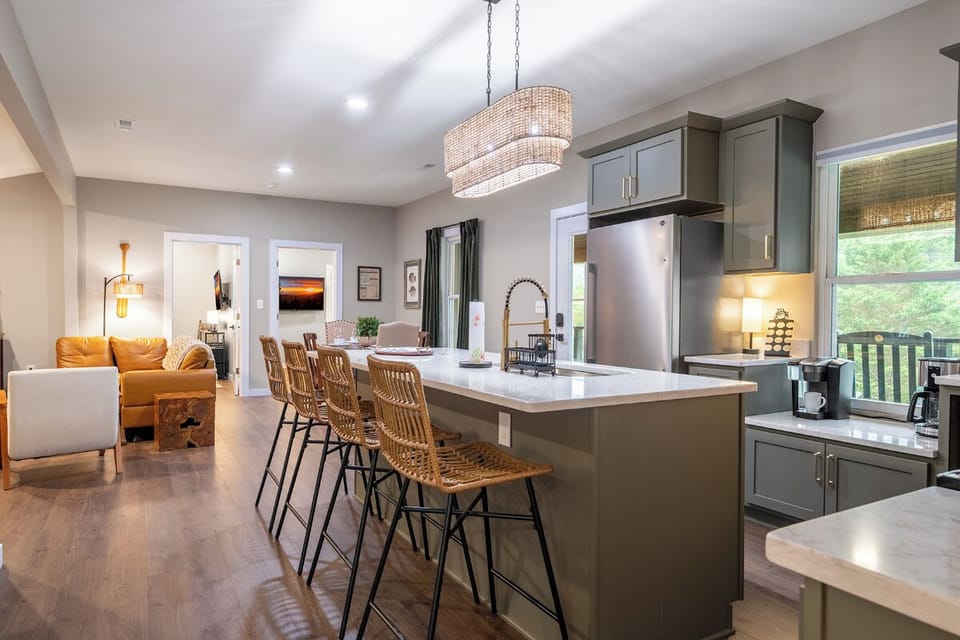 Step into your open-concept gathering space where the kitchen island becomes your social hub. Natural light pours in while you sip morning coffee at the counter, surrounded by modern finishes and cozy seating areas perfect for unwinding together.