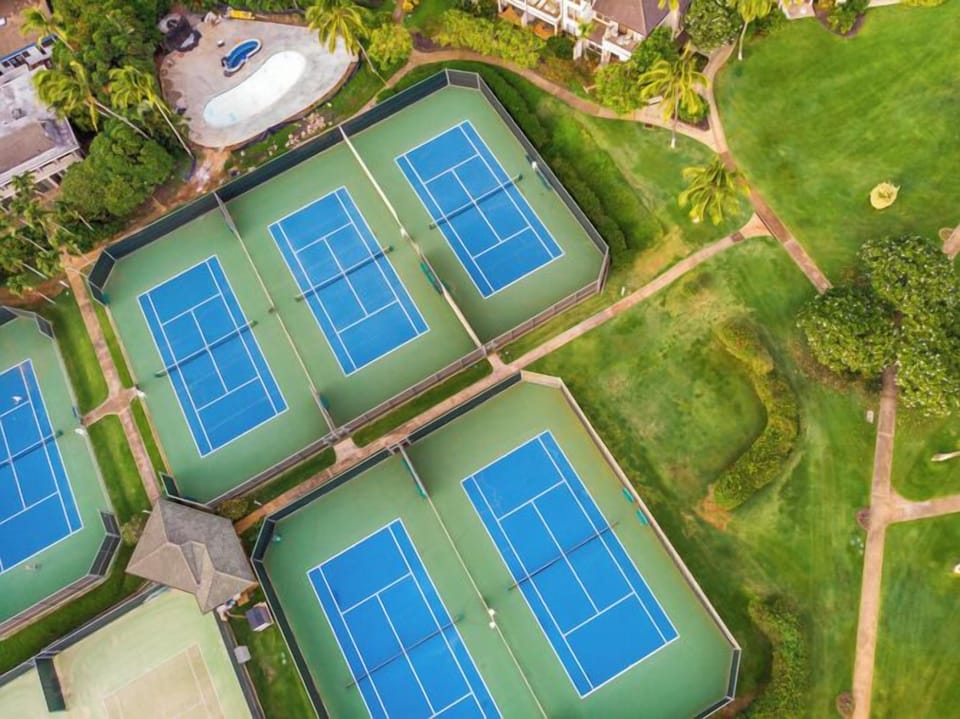 Aerial view showcasing the property's tennis courts surrounded by lush green grounds and tropical landscaping.