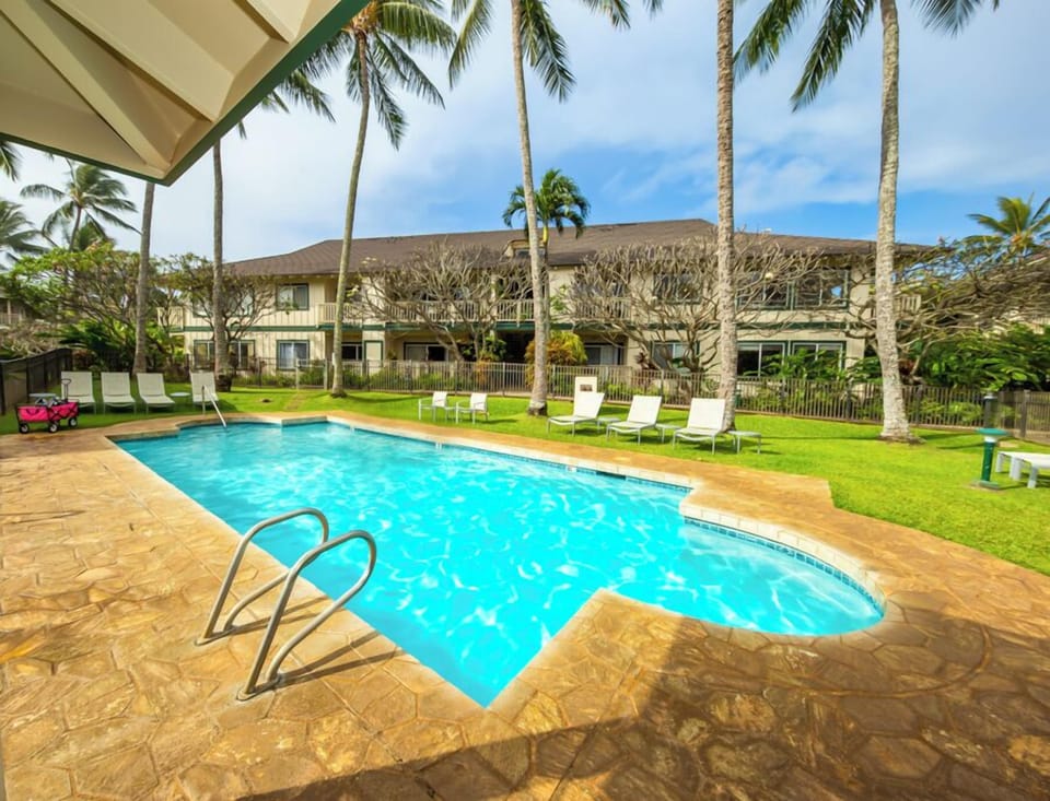 The sparkling pool set among swaying palms and lush grass, with the main building as your peaceful backdrop and loungers ready for your tropical escape.