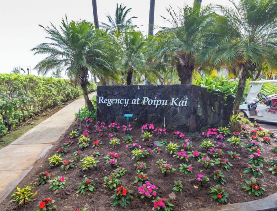The welcoming entrance sign greets visitors to Regency at Poipu Kai, set against lush tropical landscaping with vibrant flowers.