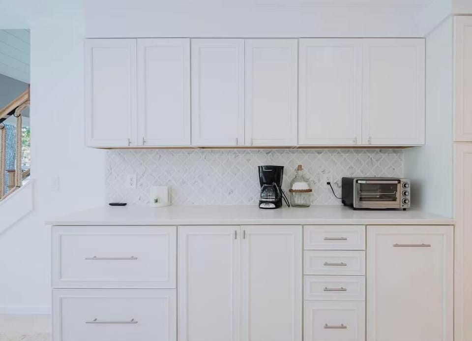 Bright white cabinetry and sleek marble backsplash create a crisp, clean space where you can brew morning coffee and prep light meals with ease.