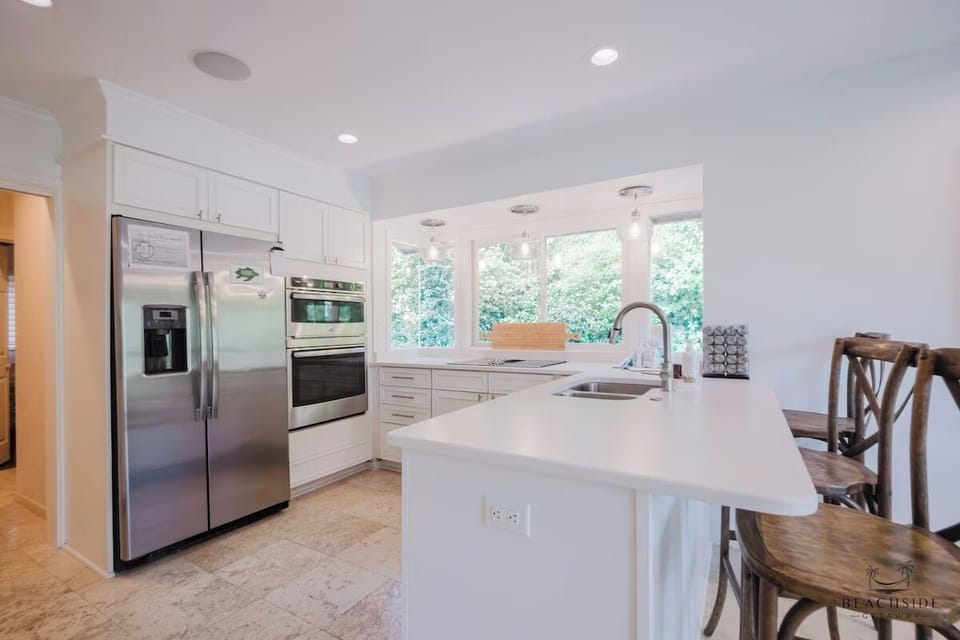 Picture yourself preparing meals in this bright, fully equipped kitchen featuring stainless steel appliances, ample counter space, and a large island—all illuminated by natural light from lush garden views.