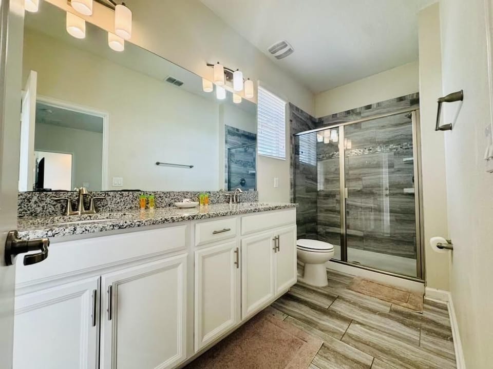 Granite countertop spans double sinks with brushed nickel fixtures in a bathroom featuring wood-tone tile and glass shower doors.