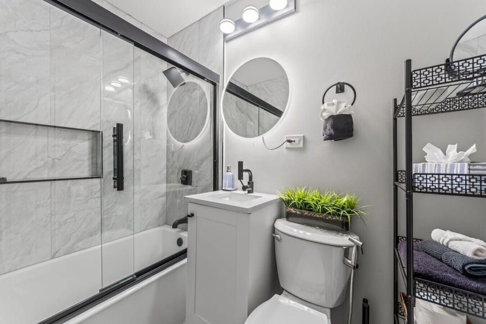 Freshly updated bathroom with a glass-enclosed tub and shower, backlit mirror, and convenient towel storage.