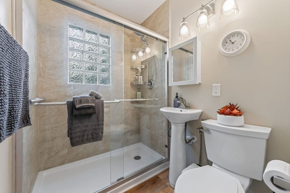 The full bathroom includes a walk-in shower, pedestal sink, and fresh towels.