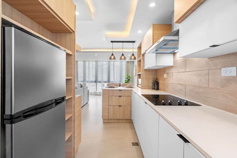 Contemporary galley kitchen with a full-size refrigerator, cooktop, range hood, and ample storage.