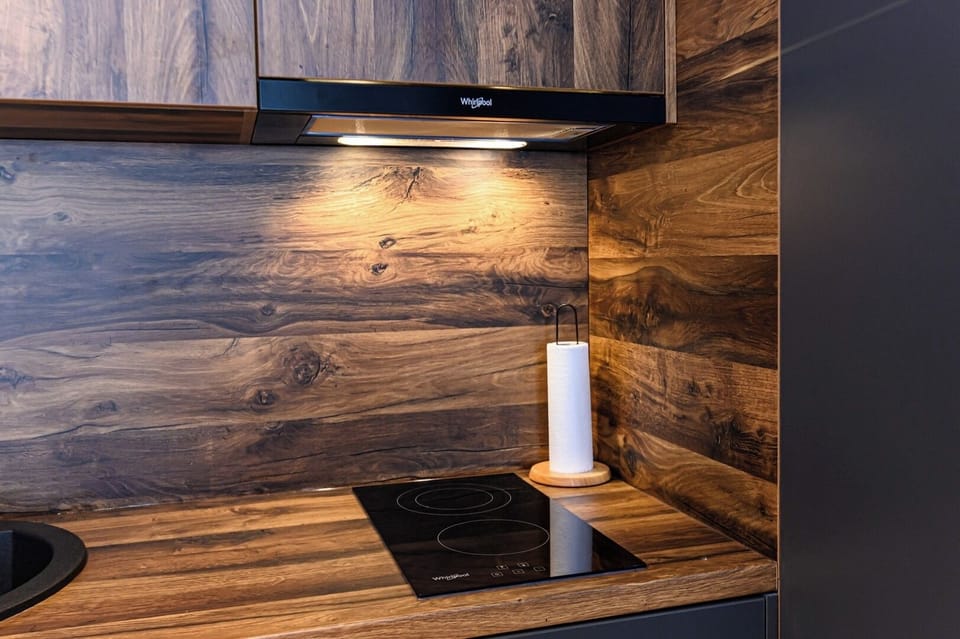 Whirlpool 2-ring induction hob set flush into a solid wood worktop. Warm walnut backsplash panelling and paper towel holder. Compact, well-integrated kitchen in Grand Chalet Suite 1, Poiana Brasov.