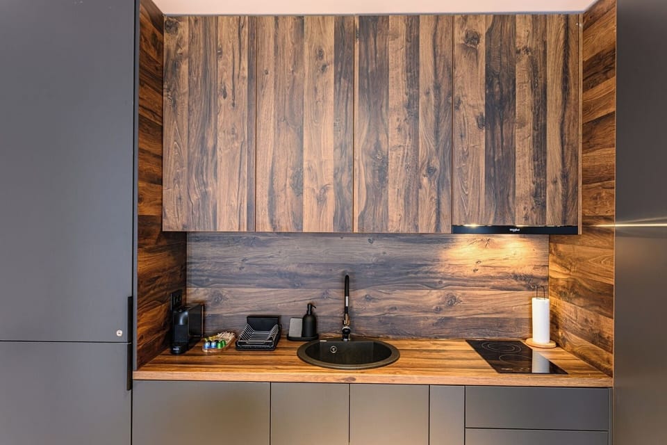 Round undermount sink with matte black tap set into a solid wood worktop against a full walnut wood backsplash panel. Dark anthracite cabinetry throughout Grand Chalet Suite 1, Poiana Brasov.