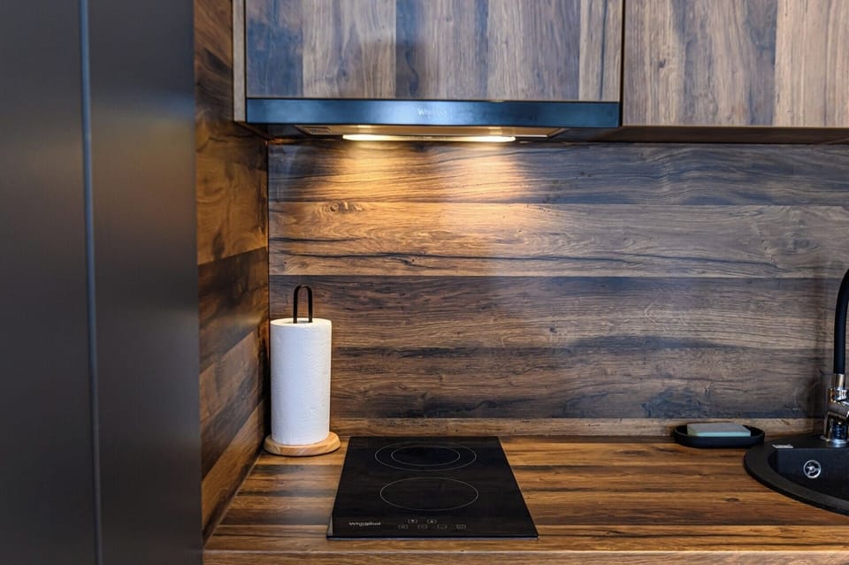 Whirlpool 2-ring induction hob close-up, flush-mounted into the solid wood worktop with rustic wood backsplash behind. Compact, precise kitchen integration in Grand Chalet Suite 2, Poiana Brasov resort.