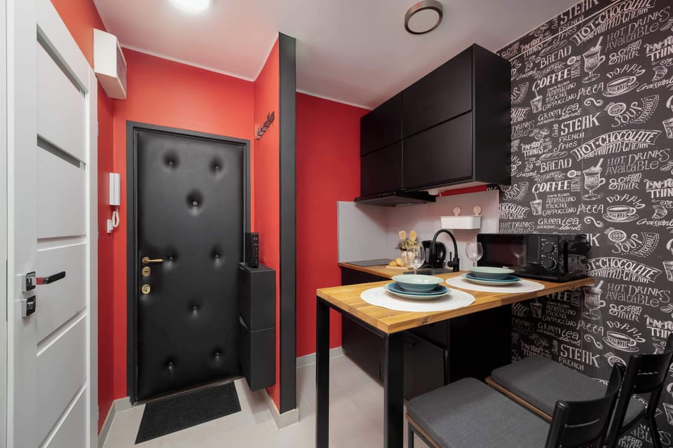 Modern kitchenette with wooden countertop, dark cabinets, dining area, and striking black-and-white patterned wall.