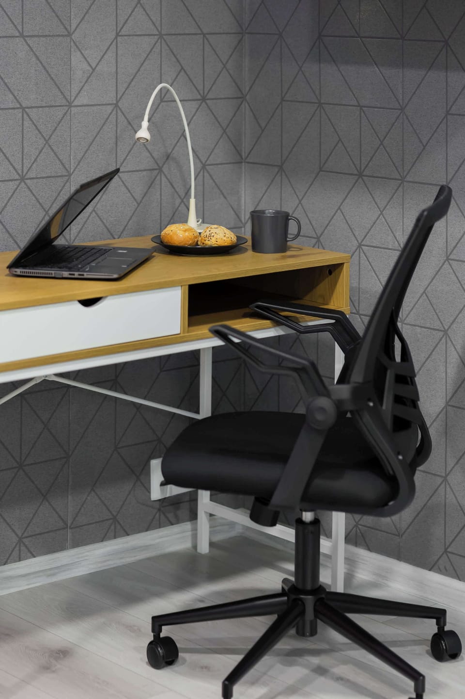 Compact workspace with a desk, office chair, computer monitor, and patterned wall.