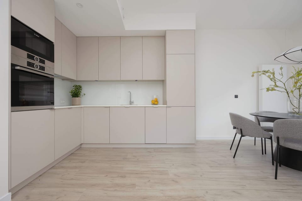 A functional kitchenette area is fitted with light-colored cabinetry and modern appliances. A dining table with dark chairs is conveniently situated just adjacent to the cooking space.