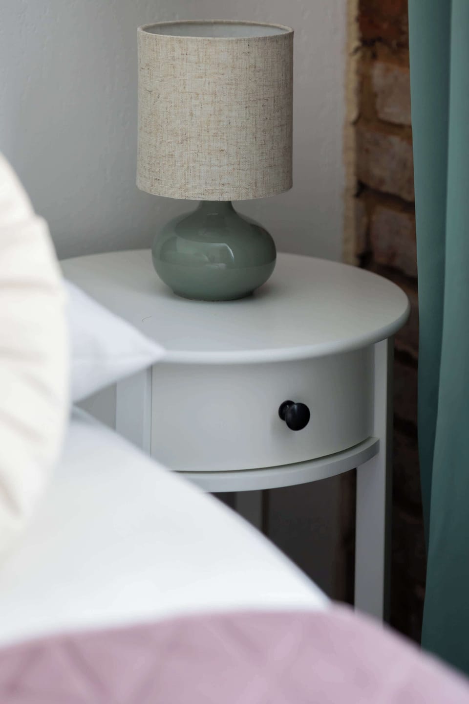 A small bedside table holds a decorative lamp and vase. The white furniture gives the room a modern look.
