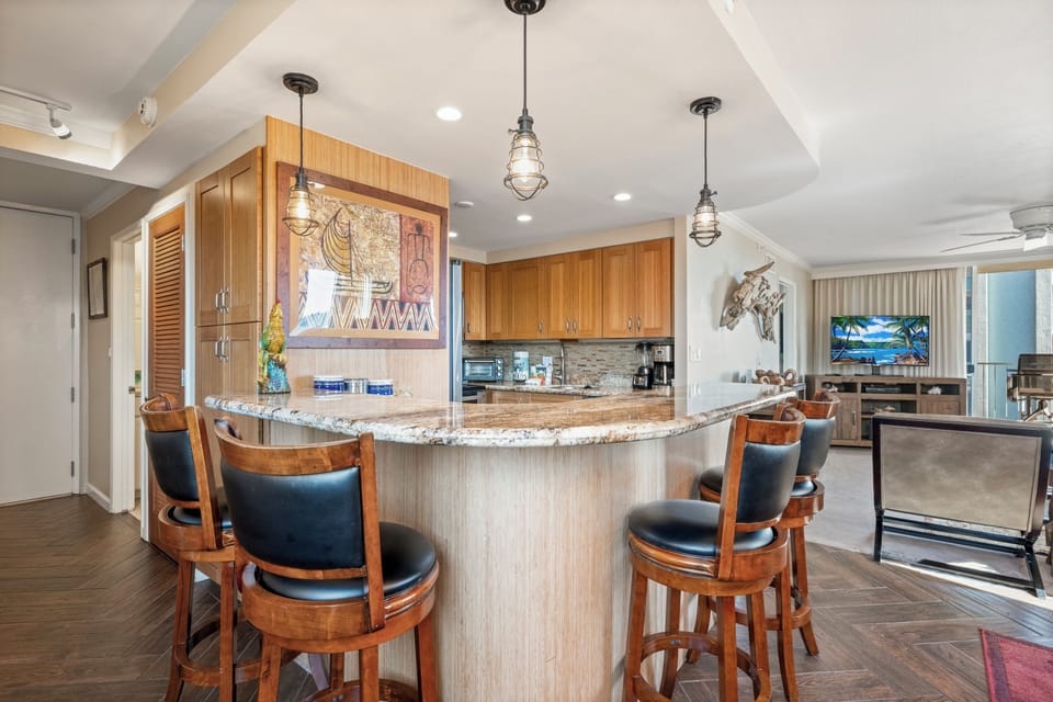 Gather at the curved breakfast bar with granite counters and warm wood tones, where industrial pendant lighting sets a welcoming vibe for your morning coffee or evening cocktails together.