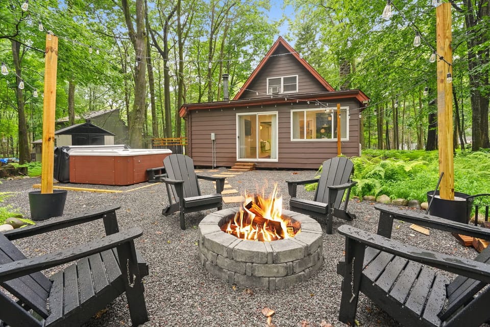 Backyard fire pit and 6-seat hot tub glowing at dusk behind the A-frame — Pocono Mountains cabin rental for 6