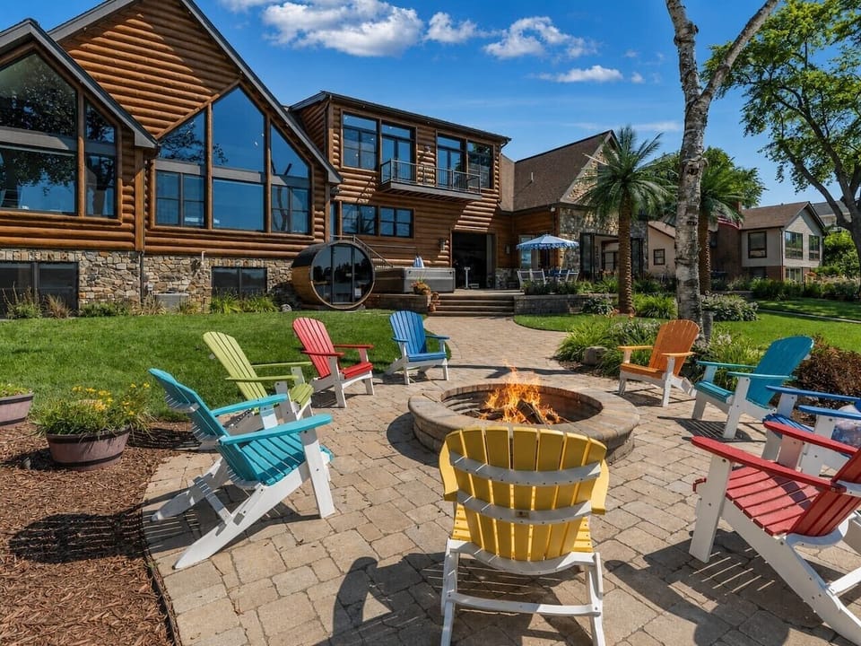 Resort-style backyard with a stone fire pit, hot tub, barrel sauna and multiple lakefront gathering zones.