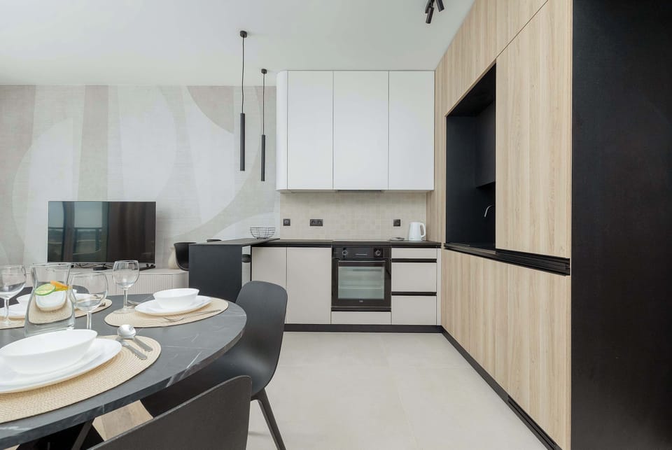 A modern kitchenette is equipped with built-in appliances and spacious cabinets. White and wood finishes create a clean look.