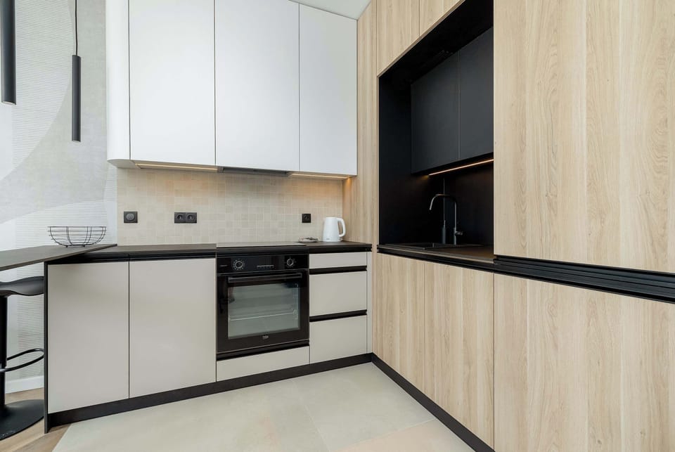 A modern kitchenette features built-in appliances and spacious cabinets. The bright design combines white and wood finishes.