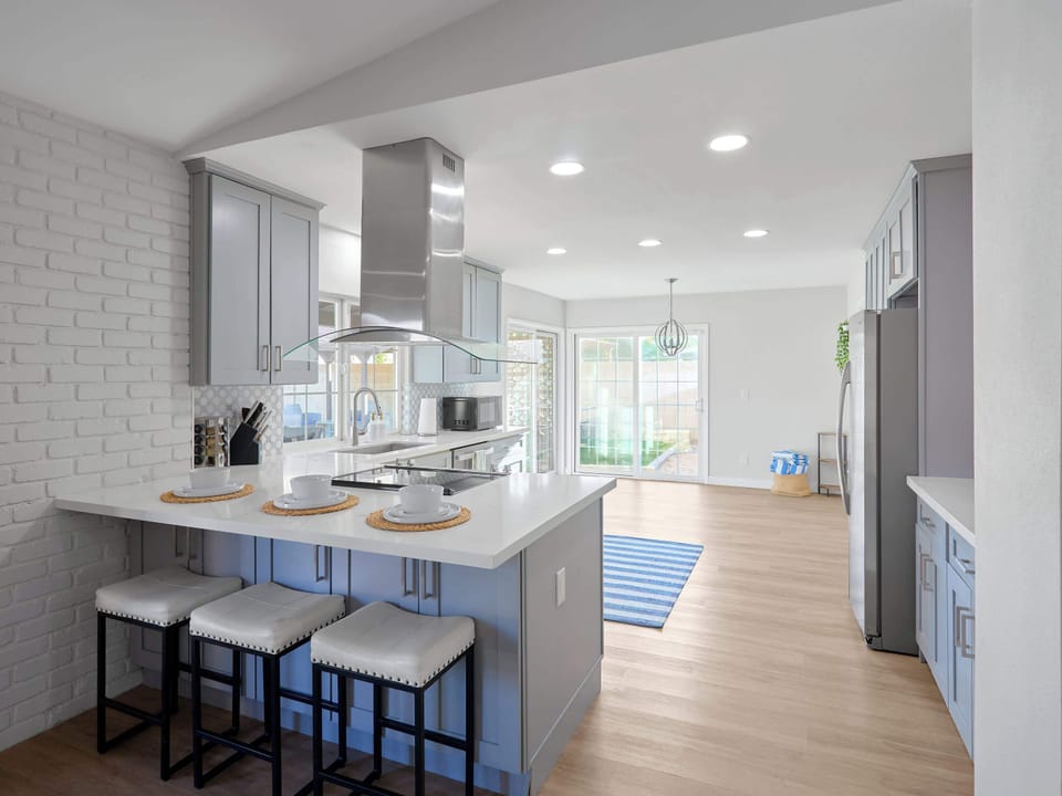 Kitchen comfort meets full function with a spacious island seating three, stainless steel appliances, and a sleek range hood, plus a coffee bar.