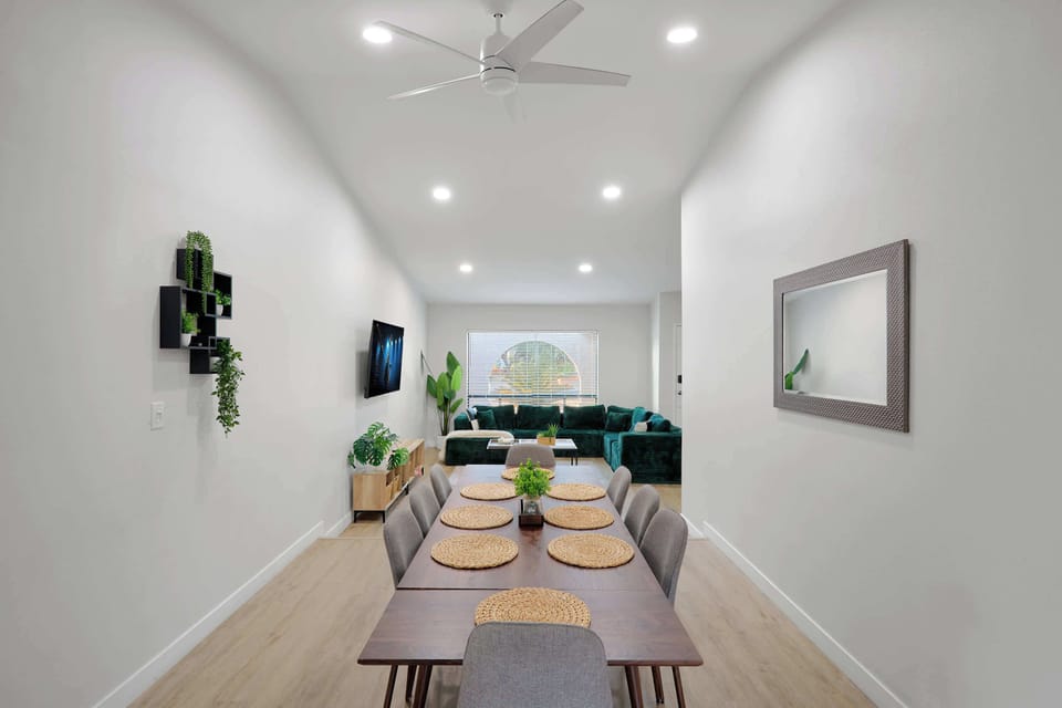 Dining area seats eight comfortably around a rich wood table, framed by a statement mirror and greenery, with an easy flow into the living room and kitchen beyond.