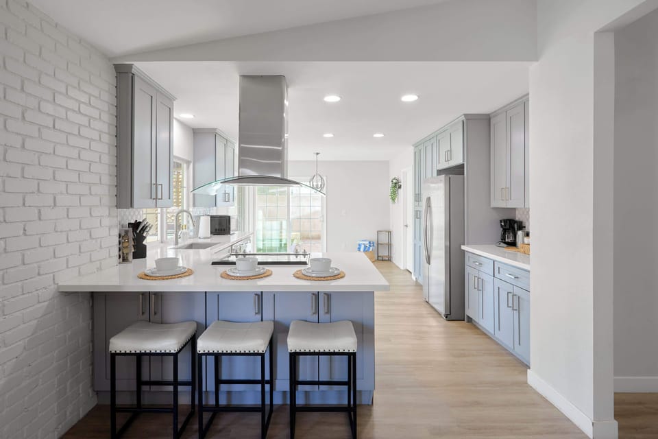 Kitchen comfort meets full function with a spacious island seating three, stainless steel appliances, and a sleek range hood, plus a coffee bar.