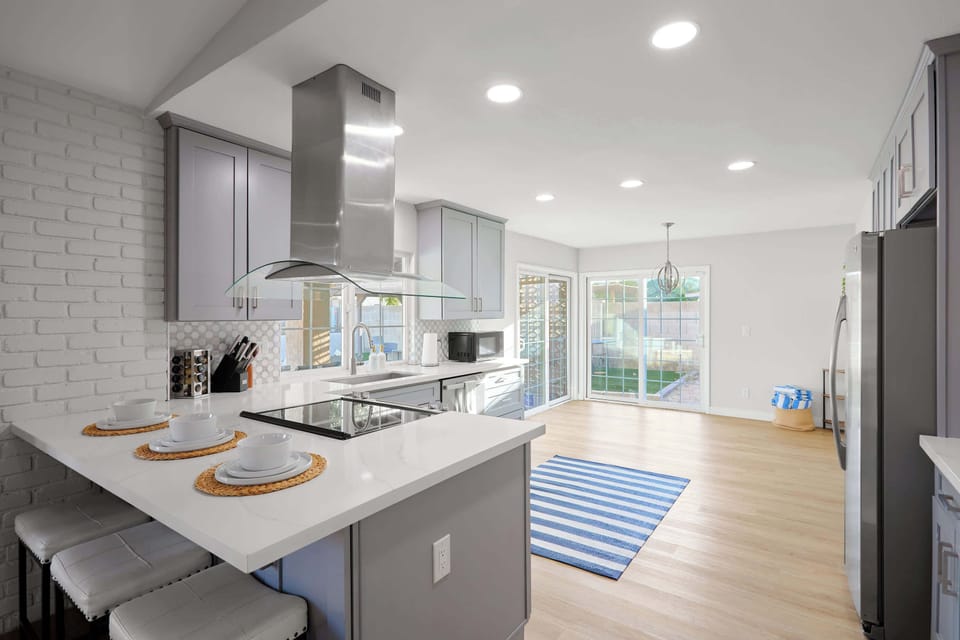 Kitchen comfort meets full function with a spacious island seating three, stainless steel appliances, and a sleek range hood, plus a coffee bar.